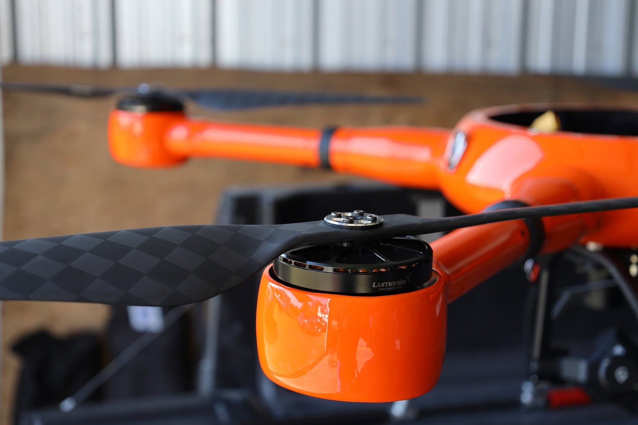 Close-up detail of Sky Monkey Media FPV racing drone — orange frame, carbon fiber props, Lumenier motor