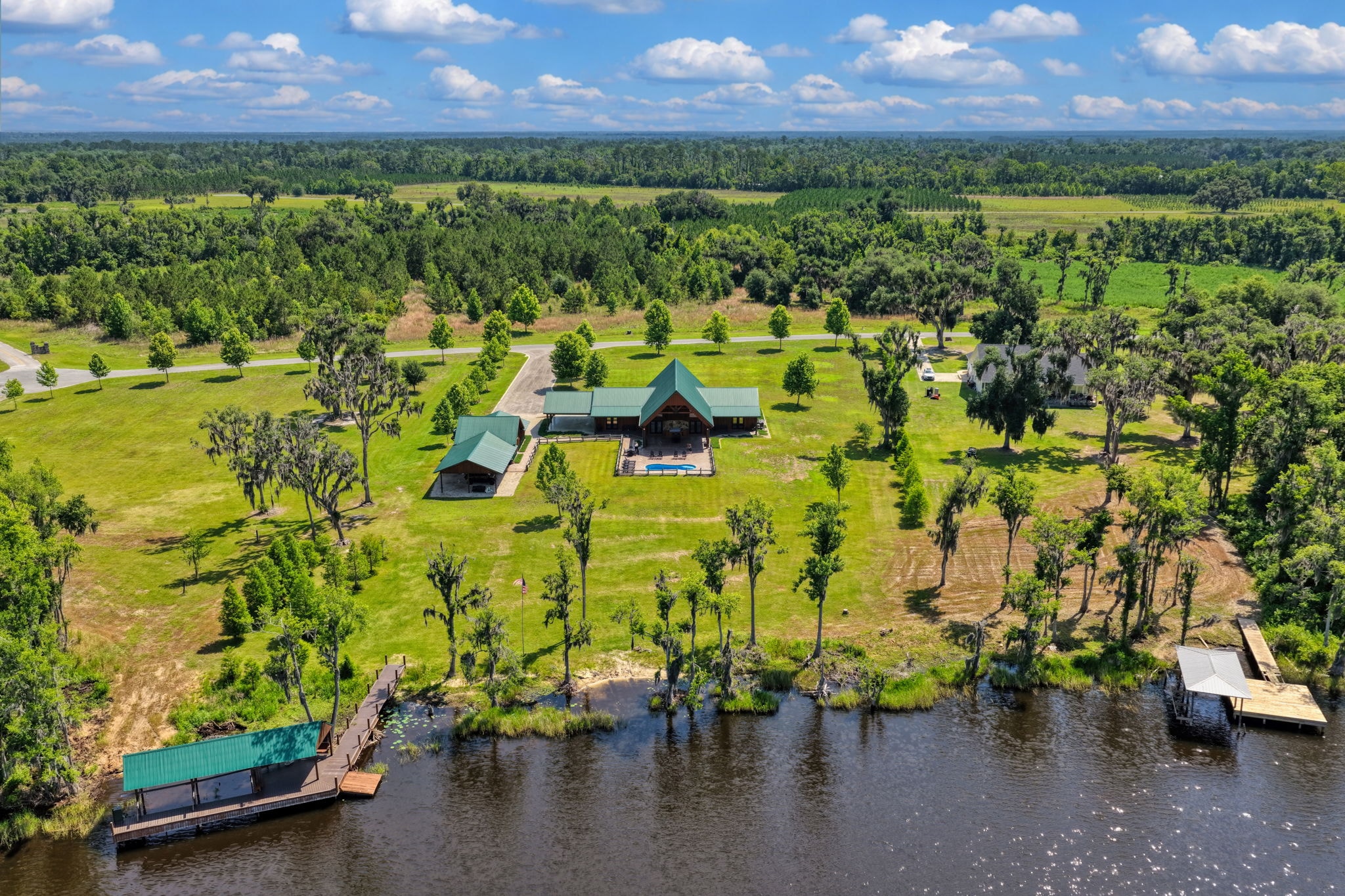 Aerial drone view of log-style riverfront estate with private dock, boathouse, pool, and acreage