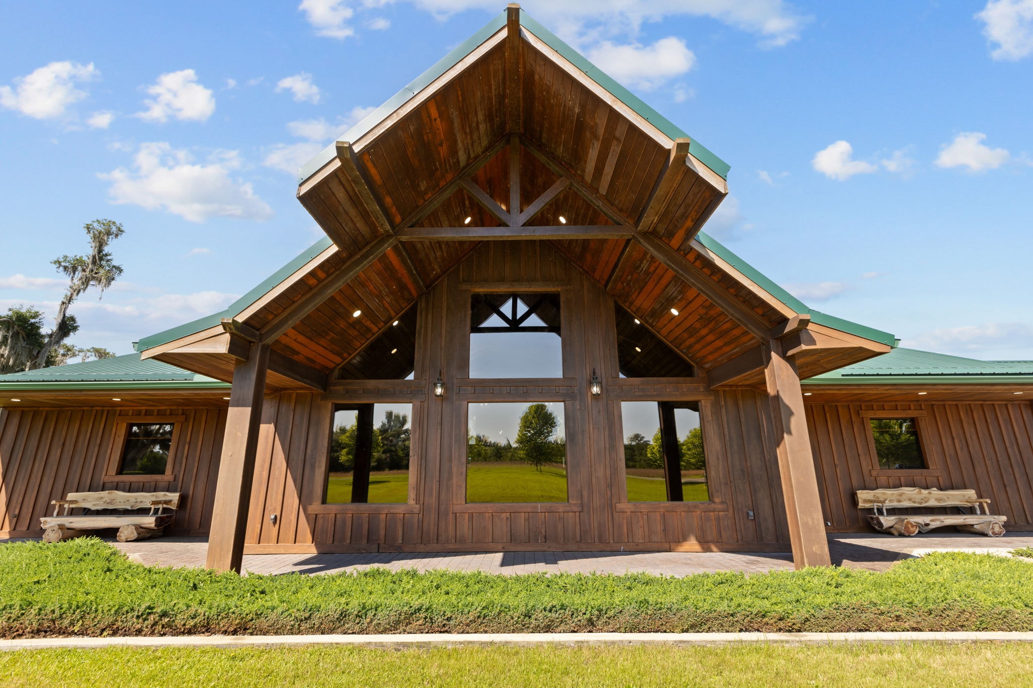 Timber-frame lodge entrance with green metal roof, exposed beam gable, and floor-to-ceiling windows