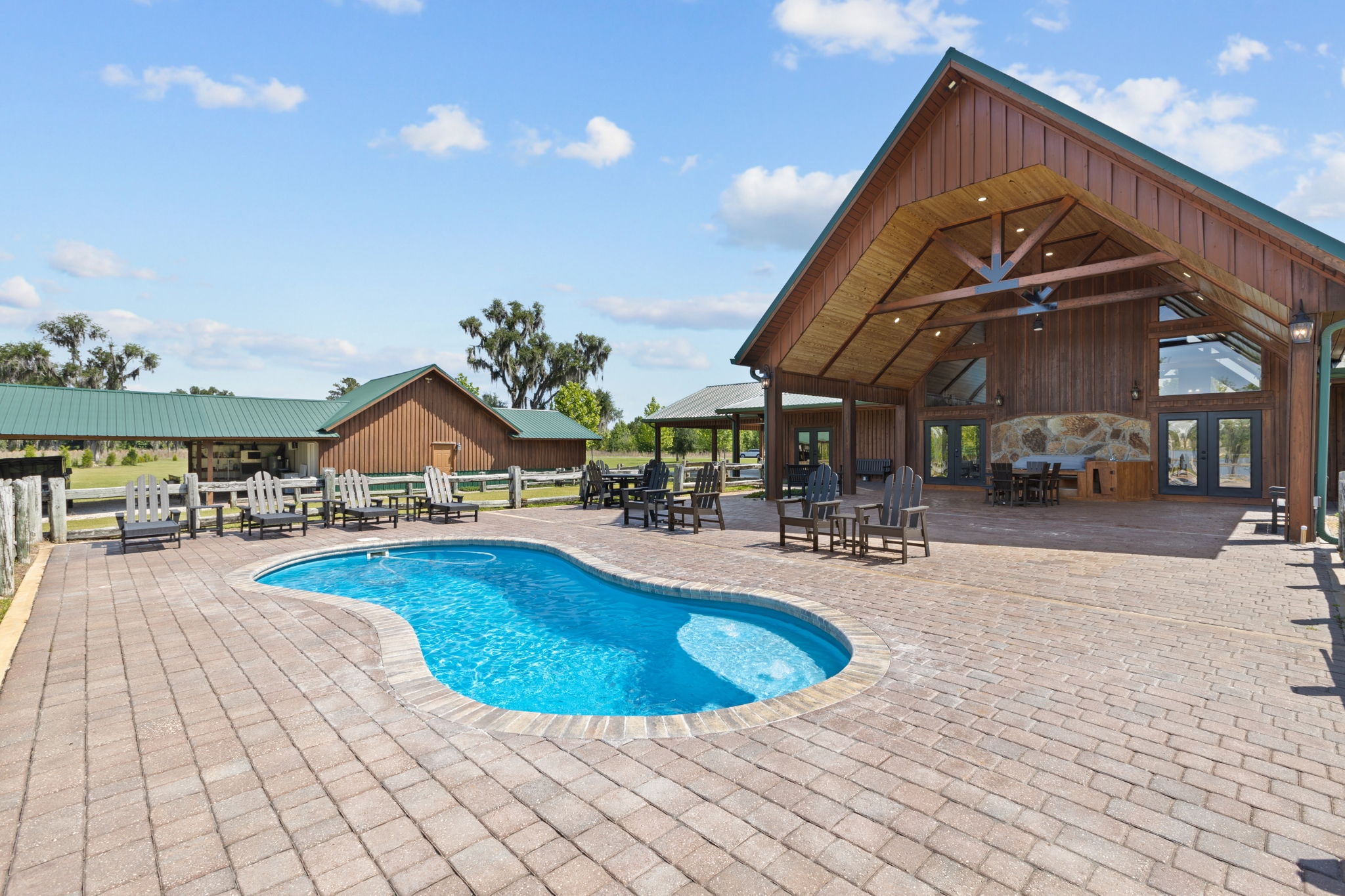 Freeform pool with paver courtyard, timber-frame pavilion, stone accent wall, and open pasture beyond