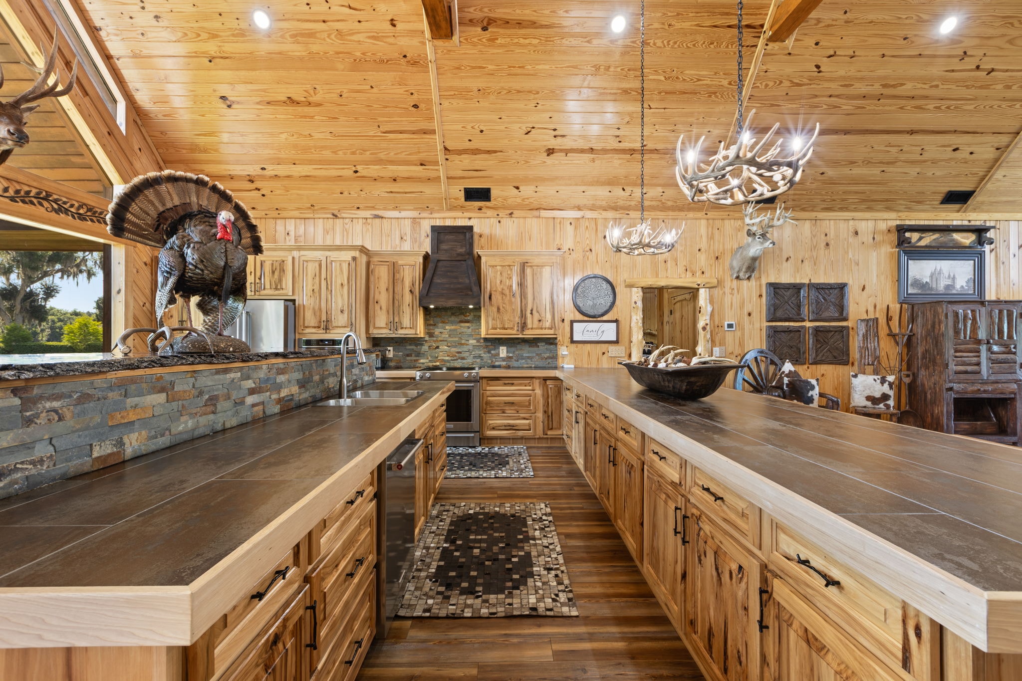Vaulted pine kitchen with antler chandeliers, hickory cabinets, stone backsplash, and trophy mounts