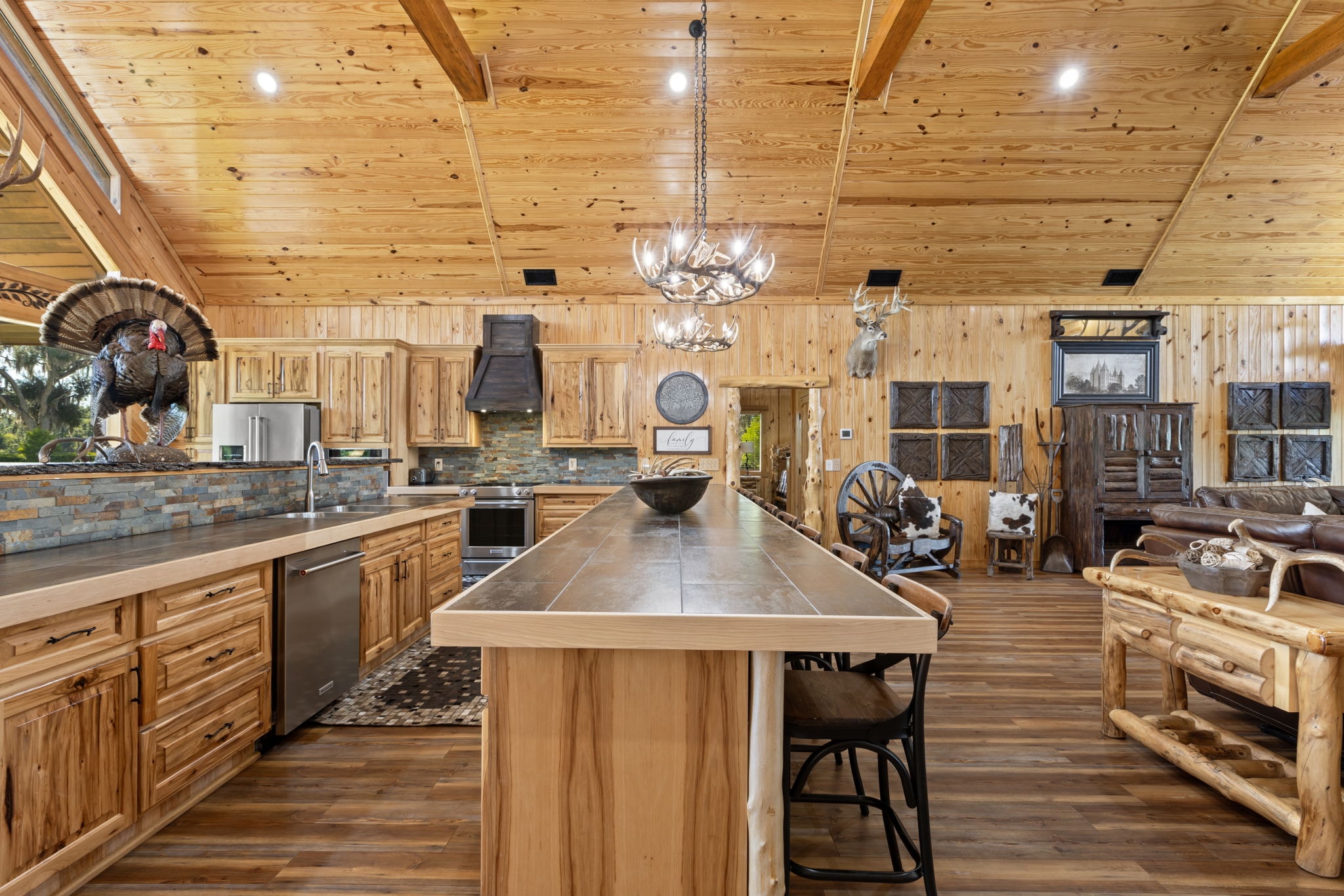 Lodge kitchen island view toward the great room with vaulted pine ceiling and antler chandelier