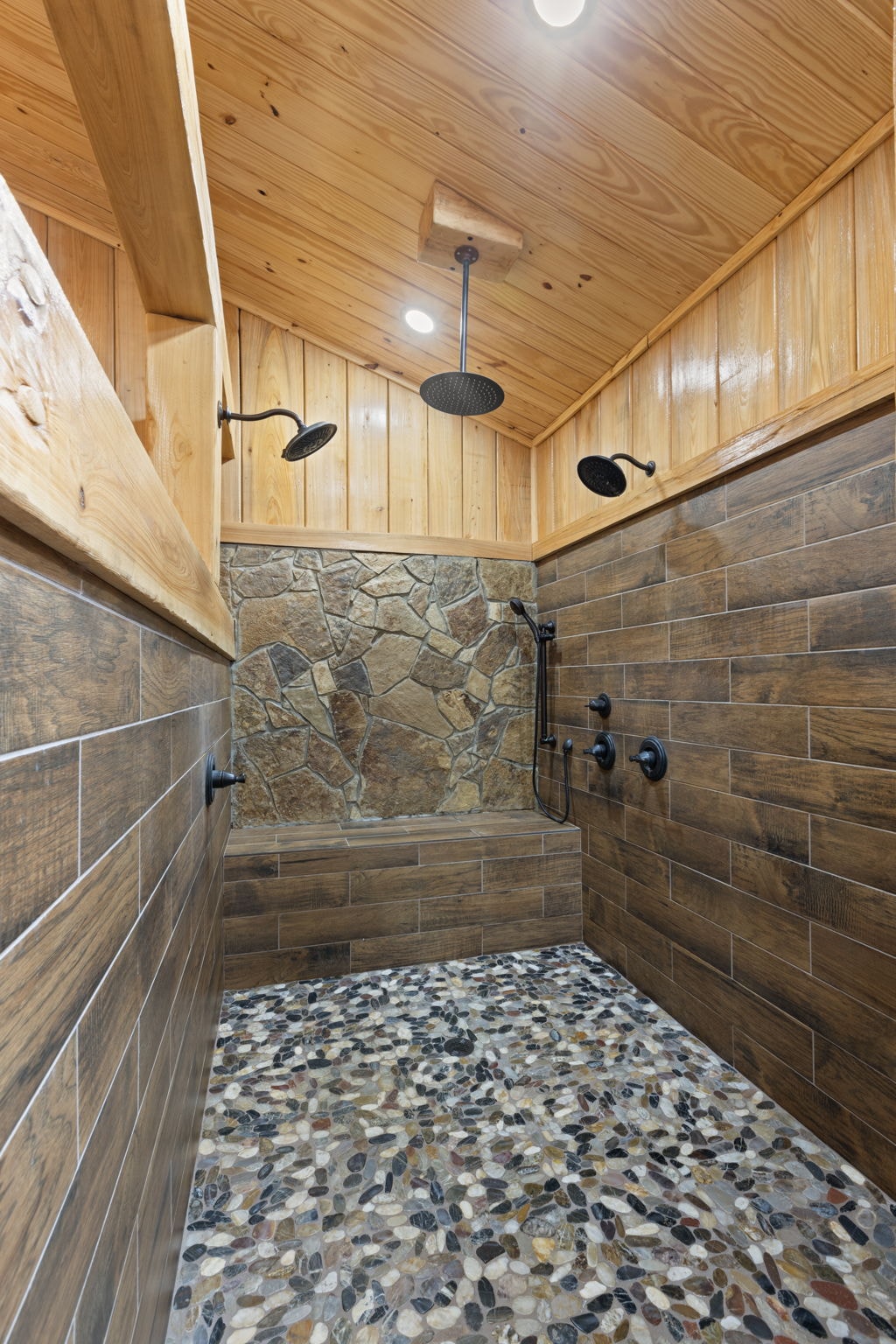 Walk-in shower with wood ceiling, stone accent wall, pebble floor, and oil-rubbed bronze fixtures