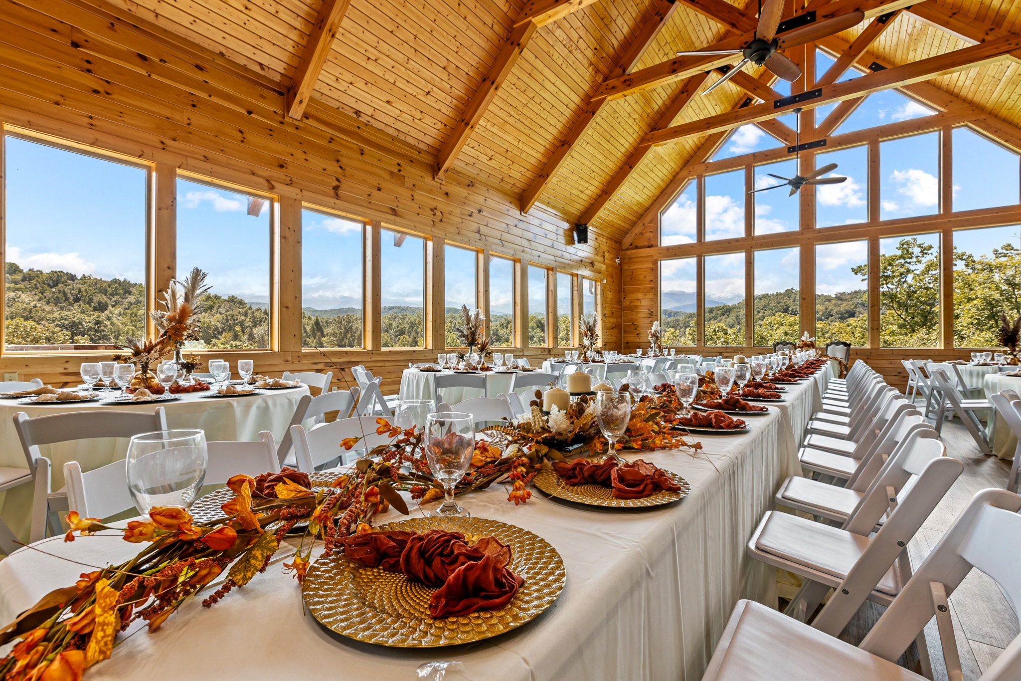 Vaulted pine reception hall with floor-to-ceiling windows and autumn-themed table settings